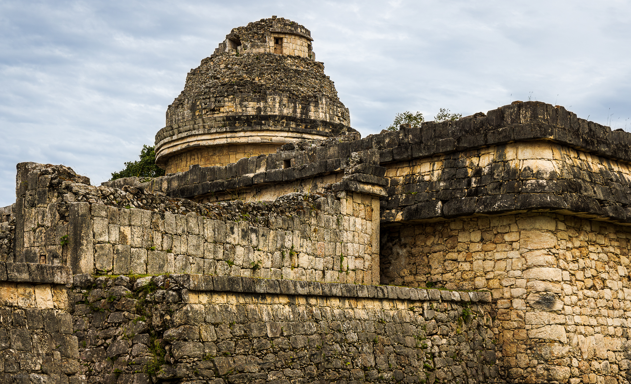 The Caracol, or Observatory, at Chichen Itza, against a backdrop of blue sky and clouds. The circular building on a large square platform, known for its astronomical significance, stands as a testament to Mayan ingenuity.