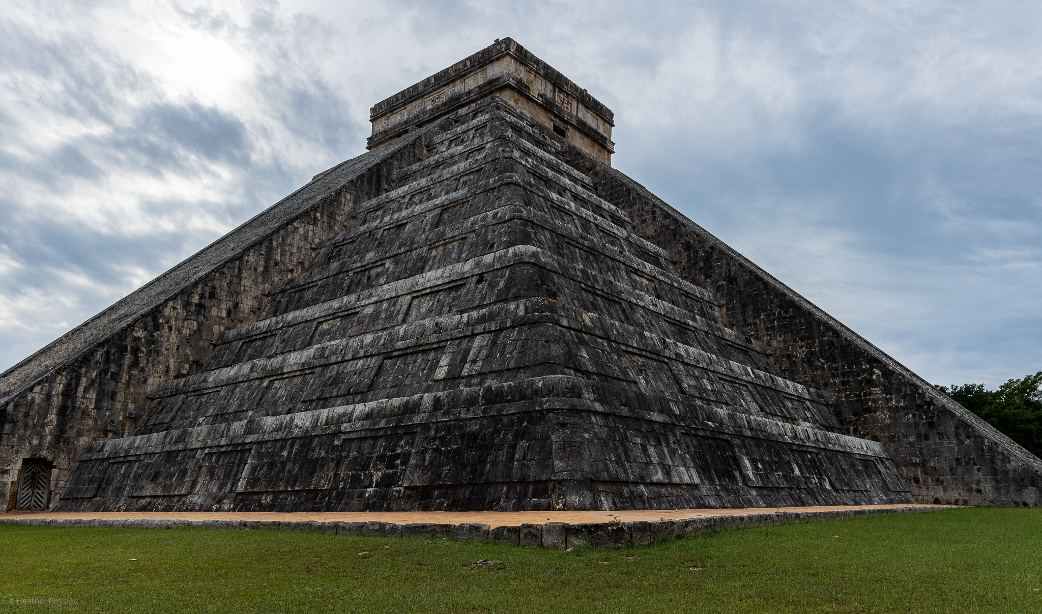The image showcases the iconic El Castillo, also known as the Temple of Kukulcan, at Chichén Itzá. This massive step pyramid stands against a cloudy sky, illustrating the grandeur of ancient Mayan architecture and the site's status as one of the New Seven Wonders of the World in Yucatan, Mexico.