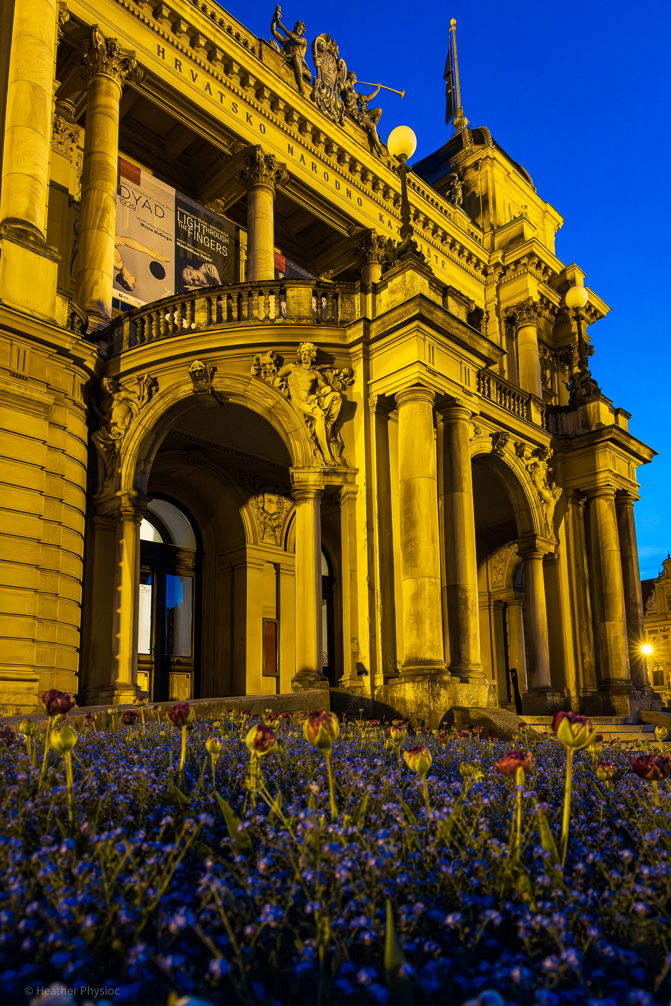 Bed of spring flowers and tulips in front of the entrance of the Croatian National Theater in Zagreb at blue hour in golden streetlight